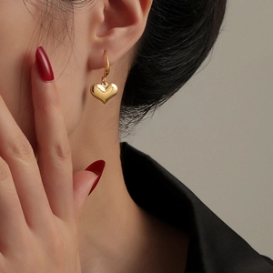 Polished gold heart drop earrings worn by a model in a minimalist French vintage style