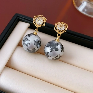 Boucles d'oreilles fleur dorées avec perle flocon de neige sur boîte en satin beige