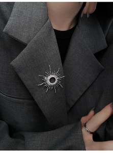Detail of silver sunburst brooch with zircons on a grey wool blazer with a silver ring