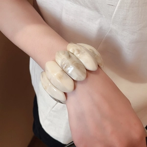 Close-up of a wide marble-pattern resin bracelet featuring elegant cream white oval segments