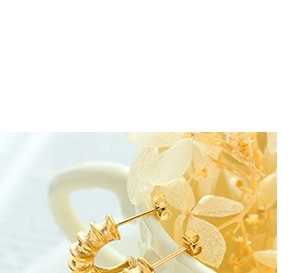 Detalle de pendiente chapado en oro con textura espiral en el borde de una taza blanca