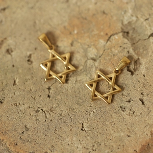 Macro shot of two gold-plated hexagram pendants on a natural stone textured background
