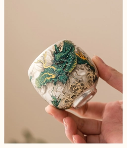 Detailed view of hand-held ceramic tea cup with green dragon and gold accents