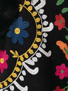 Makroaufnahme bunter Stickereien auf schwarzer Kunstfellweste mit Texturdetails