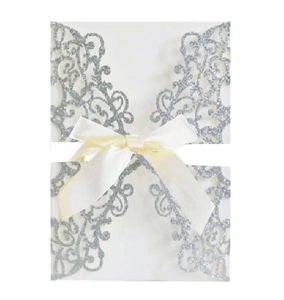Close-up of glitter silver laser-cut wedding invitation with a beige satin ribbon bow