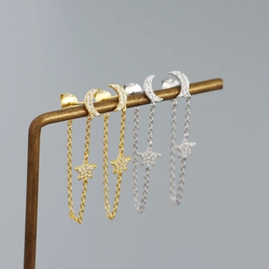Detailed view of silver and gold moon star tassel earrings with zircon inlay on a stand