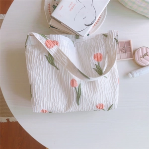 Détail du sac cabas gaufré blanc avec broderie de tulipe rose sur une table ronde