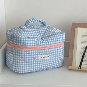 Close-up of blue checkered quilted makeup bag with pink bow and zipper detail