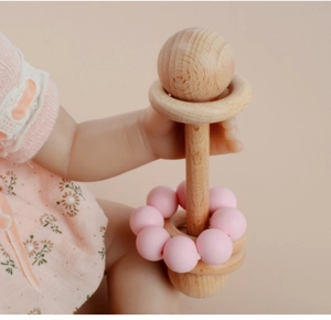 Close-up of baby grasping a beechwood rattle with pink silicone beads and wooden rings