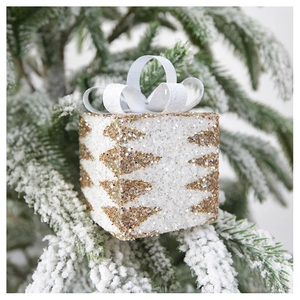Sparkling white and gold gift box ornament with a silk bow hanging on a snowy pine branch