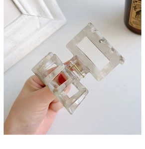 Close-up of a square marbled acetate hair claw clip showing spring mechanism and texture