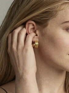 Close-up of three-layer textured C-shape gold earrings worn by a model in warm light