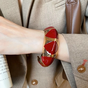 Detail of red enamel and gold vintage cuff bracelet worn on wrist with elegant blazer