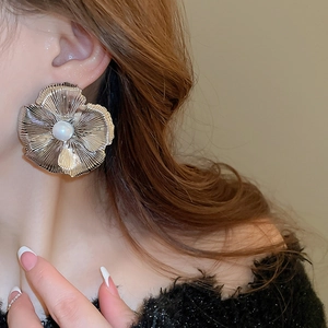 Close-up of oversized silver floral earrings with central white pearl on a model