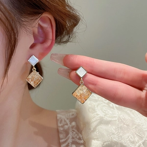 Detail of elegant gold earrings featuring square shell inlay and amber crystal pendants