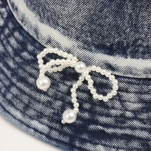 Detailed macro view of the pearl bow embellishment on dark blue denim bucket hat texture