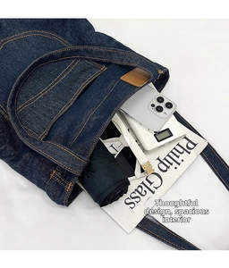 Dettaglio dell'interno spazioso della borsa in denim con cuciture arancioni e oggetti