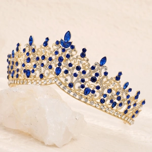 Vintage luxury gold crown with blue teardrop crystals displayed on white crystal rock