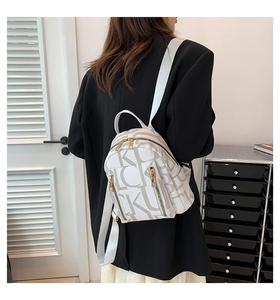 Close-up of a white leather backpack featuring a repeating letter K pattern and gold zipper