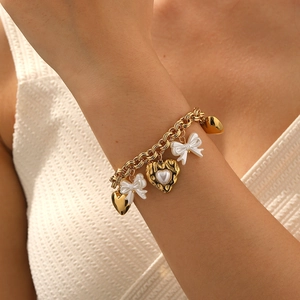 Gold chain bracelet with white pearl heart and bow pendants worn by a female model