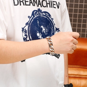Close-up of wide Cuban link bracelet with stones on wrist against a brown sofa