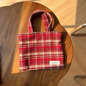 Détail d'un sac en tweed à carreaux rouges avec nœud et étiquette sur table en bois