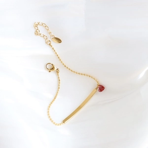Detail of gold beaded bracelet featuring a red heart stone and polished bar on silk