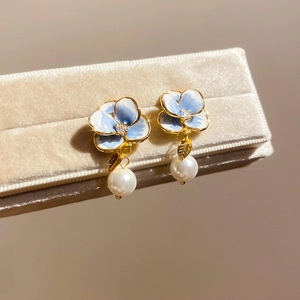 Macro shot of blue gradient flower earrings with gold edges and hanging white pearls