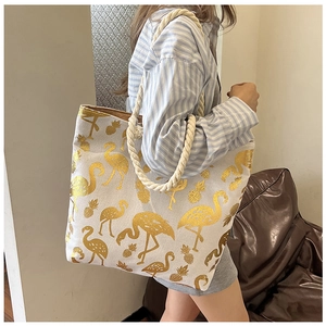 Detail of canvas tote bag featuring golden flamingo and pineapple prints with rope handle