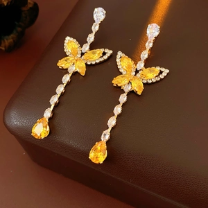 Detail of silver drop earrings featuring yellow crystals and a floral butterfly motif