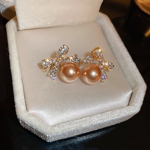 Vue macro de boucles d'oreilles nœud dorées avec strass et perles de champagne