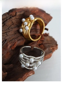 Detailed view of wave-patterned gold ring with pearls on a rustic wood stand