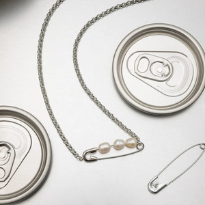 Macro detail of a silver safety pin pendant necklace with three pearls on metallic surface