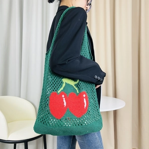 Green knitted mesh tote bag with red cherry pattern shown on female model's shoulder