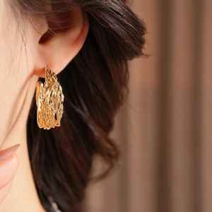 Detail view of 18K gold plated woven C-shape hoop earrings on model with metallic texture