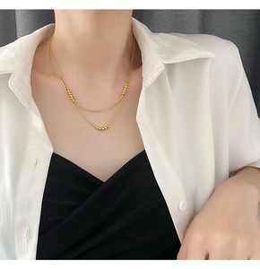 Close-up of a double-layered gold titanium necklace with minimalist beads on a model