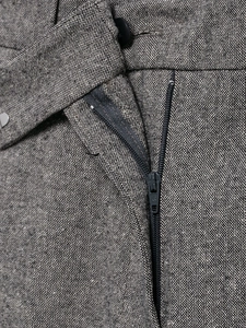 Detail of gray tweed trousers featuring a functional zipper fly and button waist closure