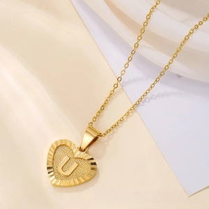 Macro shot of gold heart-shaped pendant with letter U engraving and textured metal surface