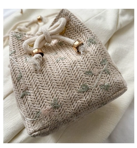 Détail d'un sac seau en paille tissé avec broderies florales et fermeture à cordon