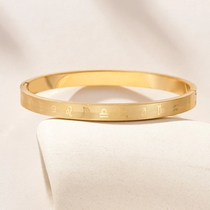Gold stainless steel zodiac bangle with engraved symbols on a minimalist platform