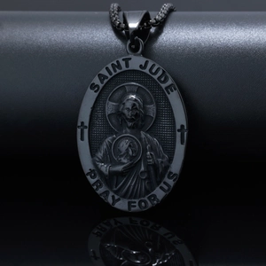 Macro shot of gunmetal Saint Jude religious pendant with engraved prayer on black pedestal