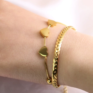 Close-up of double-layer gold stainless steel bracelet with heart charms and curb chain links