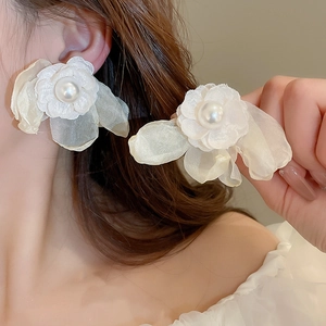 Detail of white fabric flower earrings with a glossy central pearl on a female model