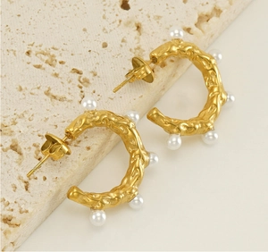 Détail de boucles d'oreilles créoles dorées avec texture lave et perles blanches