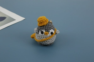 Detailed knit texture of a handmade grey penguin crochet keychain with yellow hat