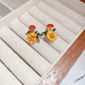 Macro shot of orange flower earrings with green leaves and small crystals in a jewelry box