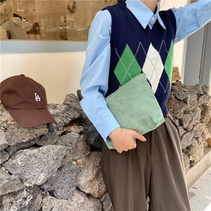 Close-up of a light green corduroy makeup pouch held by a model in casual knitwear