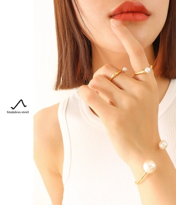 Detail shot of pearl rings and cuff bracelet in gold stainless steel on model's hand