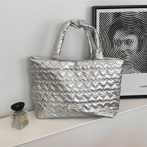 Detail of silver quilted heart tote bag with brand label on a minimalist white table