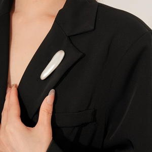 Minimalist pearl white oval brooch pinned on a black suit lapel for elegant business style